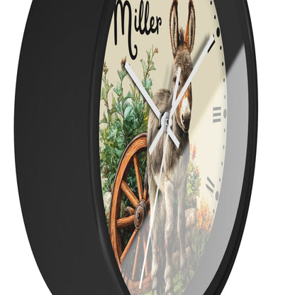 A round wall clock with a black frame and a printed western-style dial showing a donkey, green foliage, and a wooden wagon wheel. The word 'Miller' appears at the top of the dial.