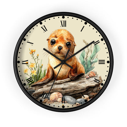 A round wall clock with a black frame and a cream-colored face featuring a detailed illustration of a seal pup sitting on a log with seashells and sea plants. The clock has black Roman numerals and black hands.