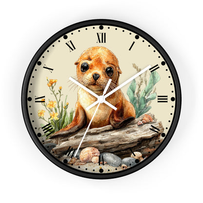 A round wall clock with a black frame and a cream-colored face featuring a detailed illustration of a seal pup sitting on a log, surrounded by flowers, shells, and rocks. The clock has black Roman numerals and white hands.