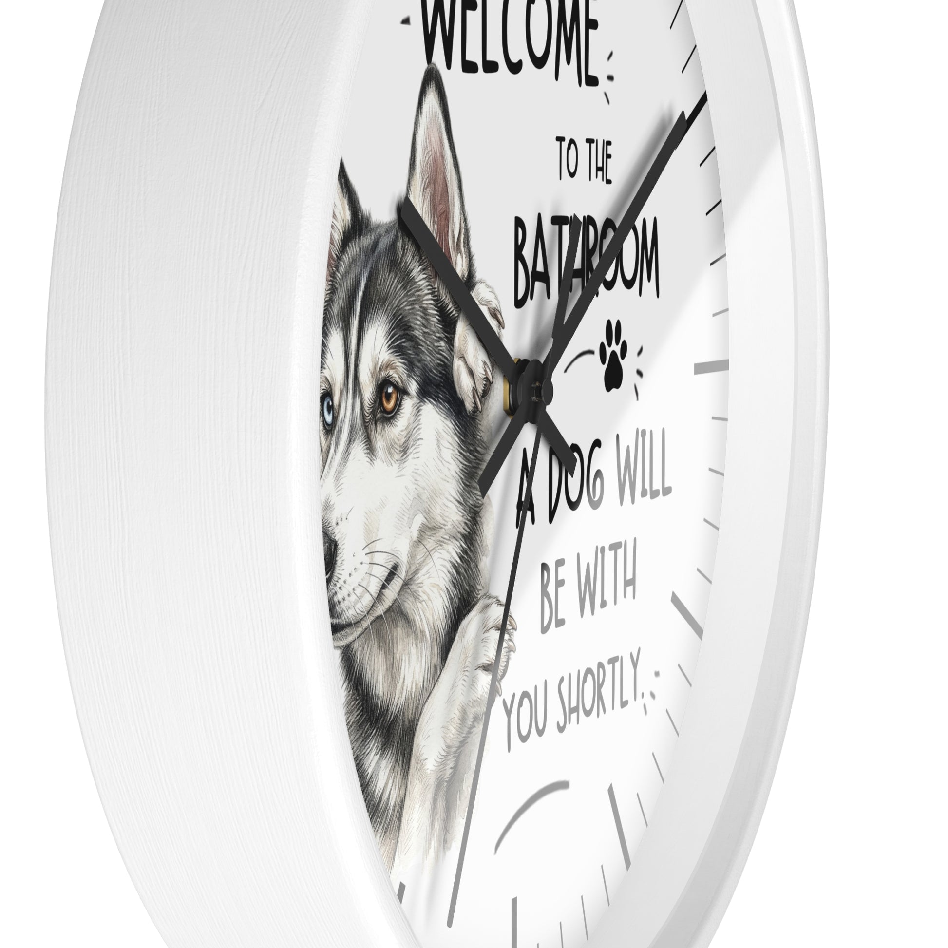 A white round wall clock with a husky dog illustration and the humorous text 'WELCOME TO THE BATHROOM A DOG WILL BE WITH YOU SHORTLY' printed on the face.
