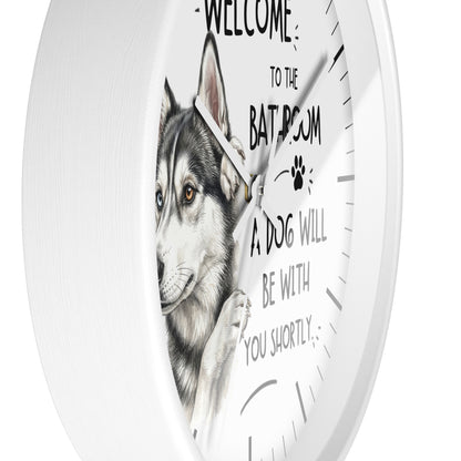 A round white wall clock with a printed illustration of a husky dog and the text 'WELCOME TO THE BATROOM A DOG WILL BE WITH YOU SHORTLY' on the front.