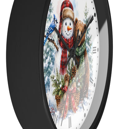 A round wall clock with a black frame and a festive winter illustration on the face, featuring a snowman in a red plaid scarf, a bluebird, a bear, pinecones, and evergreen branches.