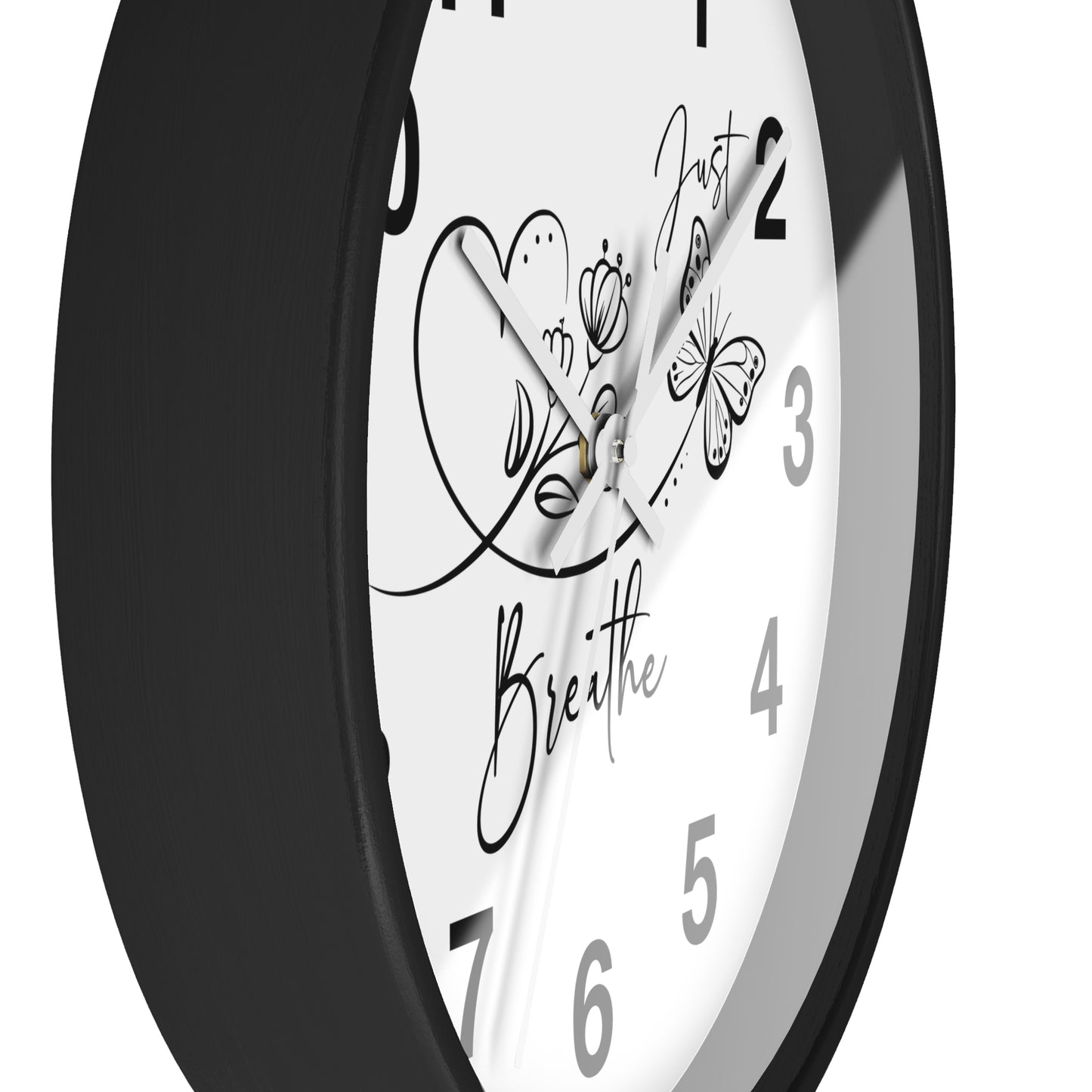 A close-up of a round wall clock with a black frame and a white face featuring black Arabic numerals and decorative script text reading 'Just Breathe' with butterfly and heart illustrations.