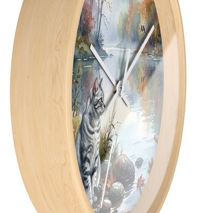 Round wall clock with a light natural wood frame and a printed scenic dial showing a gray tabby cat sitting by a reflective water scene with trees and rocks.