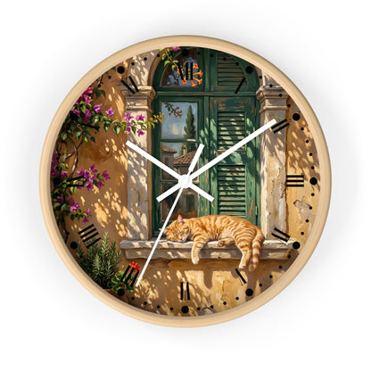 Round wall clock with a light wood frame and a printed scenic design featuring a green shuttered window, warm beige walls, purple flowers, and an orange tabby cat resting on a windowsill. White clock hands and black Roman numerals complete the look.