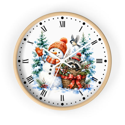 A round wall clock with a light wood frame and a white face featuring a festive winter illustration of a snowman in a red-orange hat, a raccoon in a basket, evergreen trees, and a bird, with black Roman numerals and hands.