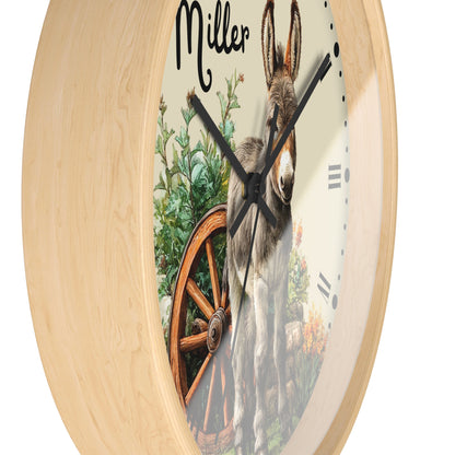 Round wall clock with a light natural wood frame and a printed face showing a donkey, greenery, and a wagon wheel. The name 'Miller' appears at the top in black script.