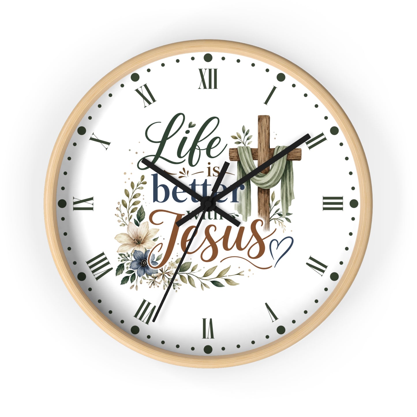 A round wall clock with a light natural wood frame and a white face. The clock face features a Christian-themed design with the text 'Life is better with Jesus' in elegant script, accompanied by a wooden cross draped with green cloth, floral illustrations, and black Roman numerals.