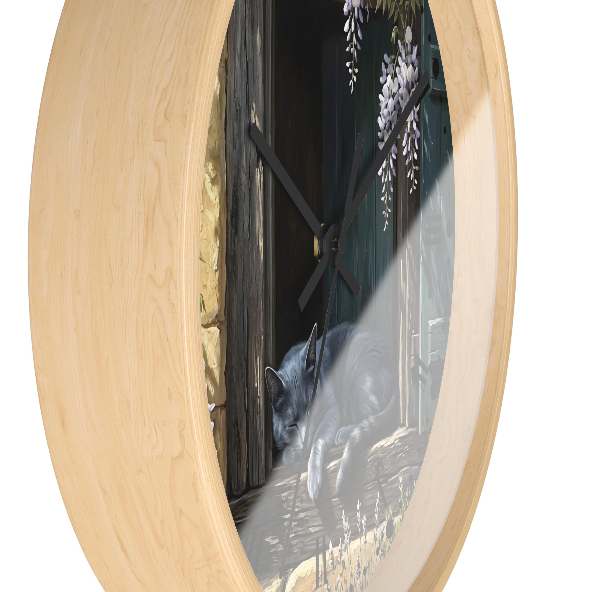 Round wall clock with a light natural wood frame and a printed scene on the face showing a gray cat in front of a dark wooden door with wisteria flowers, photographed on a white background.
