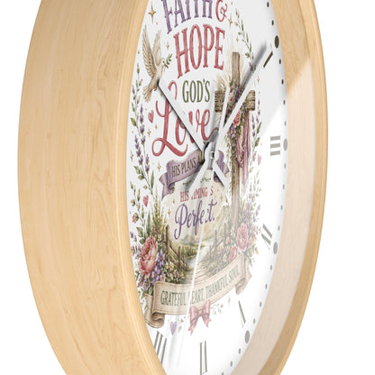 A round wall clock with a light natural wood frame and a white face featuring a Christian floral design, a cross, and the words 'Faith Hope Love God's Love His plans His guiding and Perfect.'.