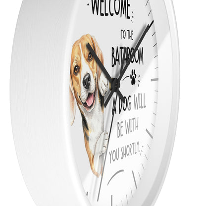 A round white wall clock with a humorous pet quote and a painted beagle illustration. The text reads 'WELCOME TO THE BATHROOM A DOG WILL BE WITH YOU SHORTLY' with a paw print, displayed against a clean white background.