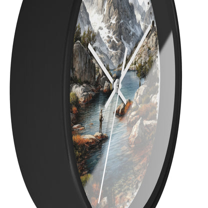 Oval wall clock with a black frame and a scenic landscape print of a mountain stream, rocks, and a fisherman, shown against a white background.