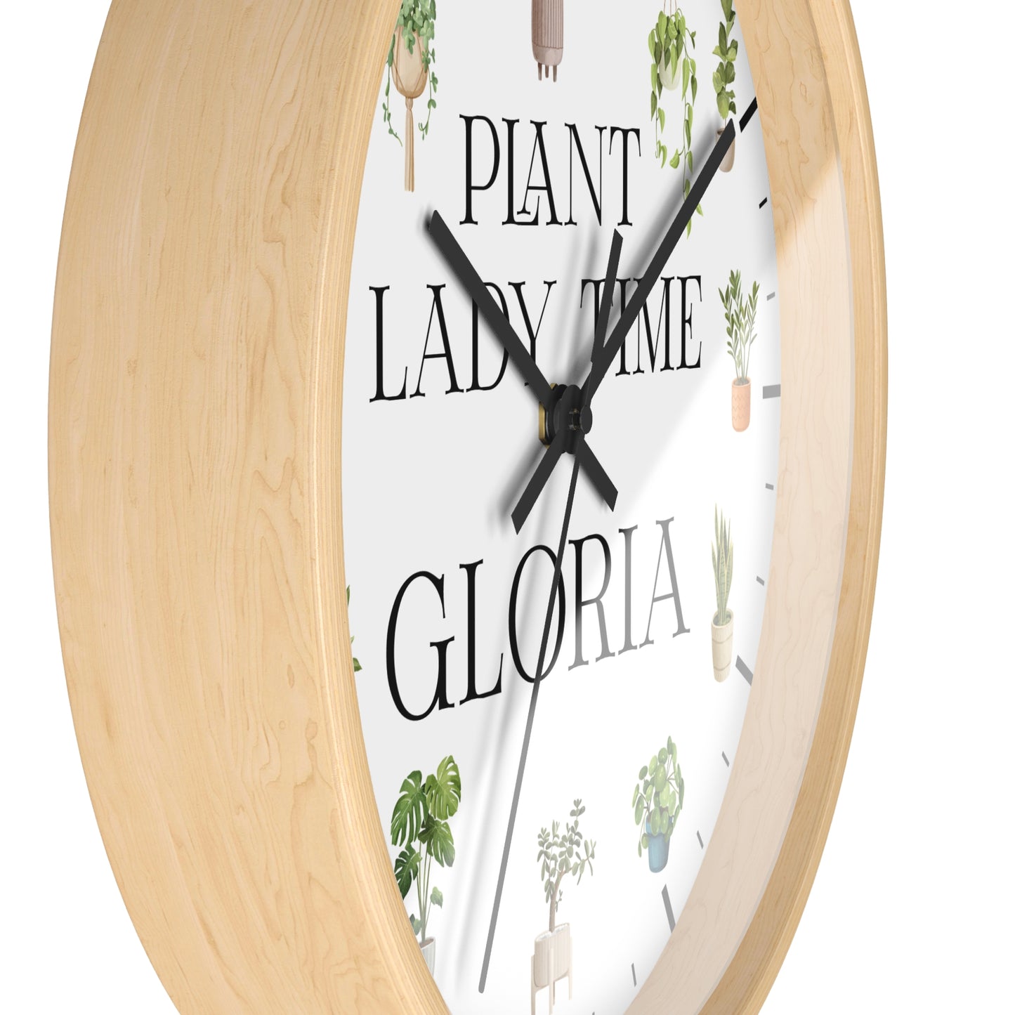 Round wall clock with a light natural wood frame, a white face, black hands, and the phrase "PLANT LADY TIME GLORIA" surrounded by small potted plant illustrations.