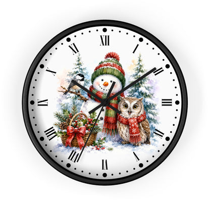 A round wall clock with a black frame and a white face featuring a winter holiday illustration of a snowman in a red and green hat next to an owl in a red scarf, with black Roman numerals and black hands.