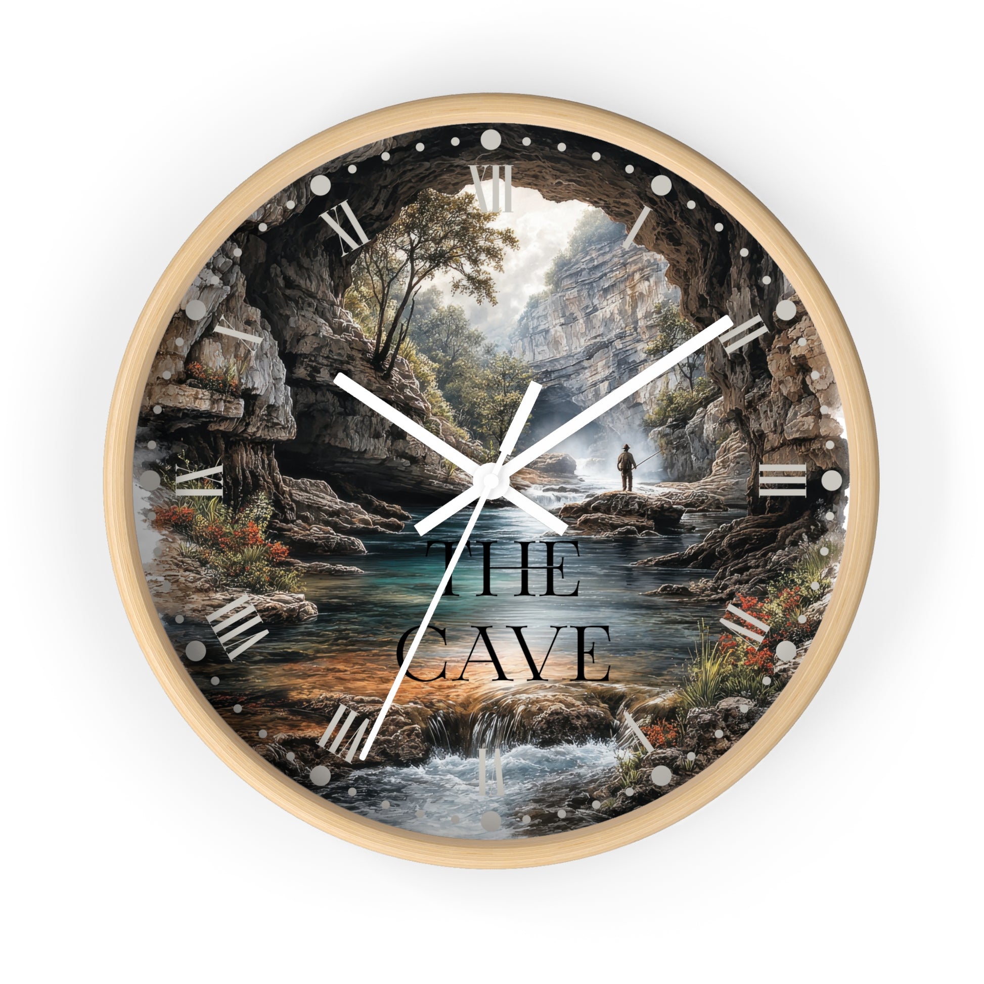A round wall clock with a light wood frame and a scenic printed dial showing a cave opening over a stream, with the words “THE CAVE” in large black letters. The clock is centered on a plain white background.