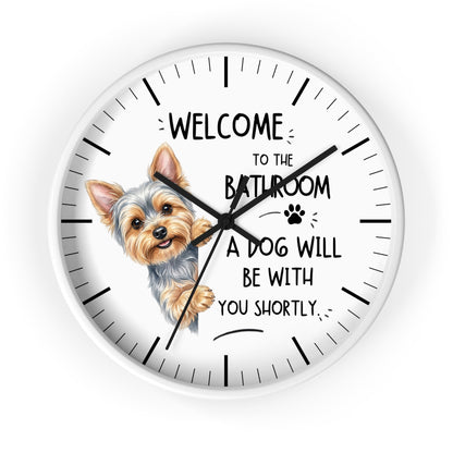 A round white wall clock with black hands and hour markers, featuring a cartoon Yorkshire Terrier illustration and the text 'WELCOME TO THE BATHROOM A DOG WILL BE WITH YOU SHORTLY.' on a white background.