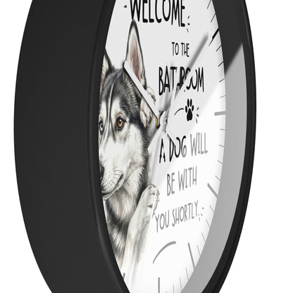 A round wall clock with a black frame and a white face featuring a husky illustration and the text 'WELCOME TO THE BATROOM A DOG WILL BE WITH YOU SHORTLY'.