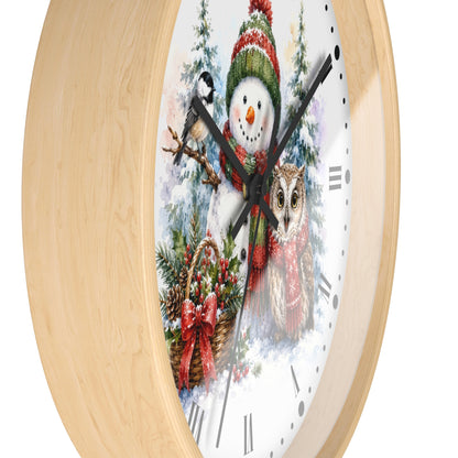 A round wall clock with a light natural wood frame and a festive winter illustration on the face, featuring a snowman, bird, owl, evergreen branches, and a red bow, shown against a plain white background.