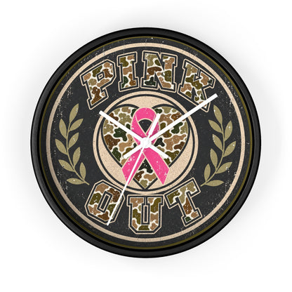 A round wall clock with a black frame and a distressed design featuring the words 'PINK OUT' in camouflage lettering, a pink ribbon heart in the center, and olive green laurel branches on a light gray background.