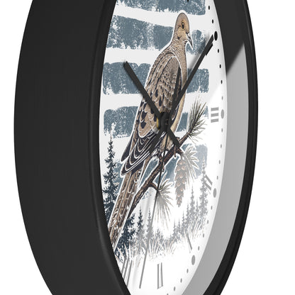 A close-up of a round wall clock with a black frame and a printed dove bird illustration on the face. The design shows a brown and beige dove perched on a pine branch against a white background with blue-gray brushstroke bands and dark tree silhouettes.