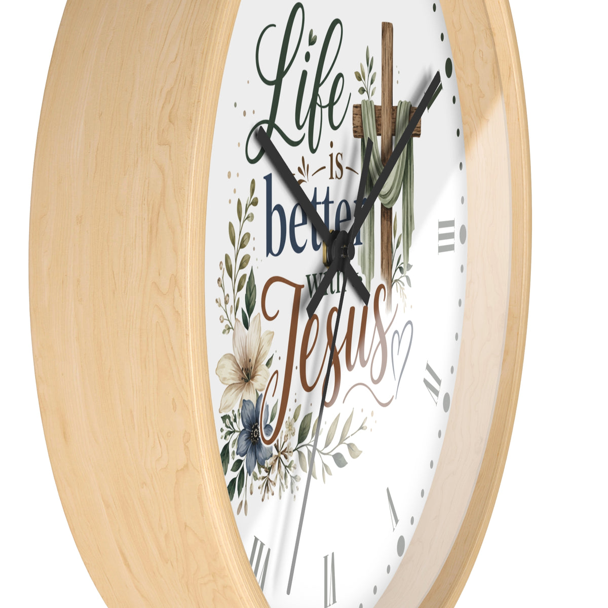A close-up of a round wall clock with a light natural wood frame and a white face featuring the phrase “Life is better with Jesus” in decorative script, along with floral and cross illustrations.