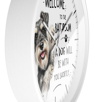 A round white wall clock with a printed illustration of a scruffy dog and humorous text that reads 'WELCOME TO THE BATROOM A DOG WILL BE WITH YOU SHORTLY' on a clean white background.