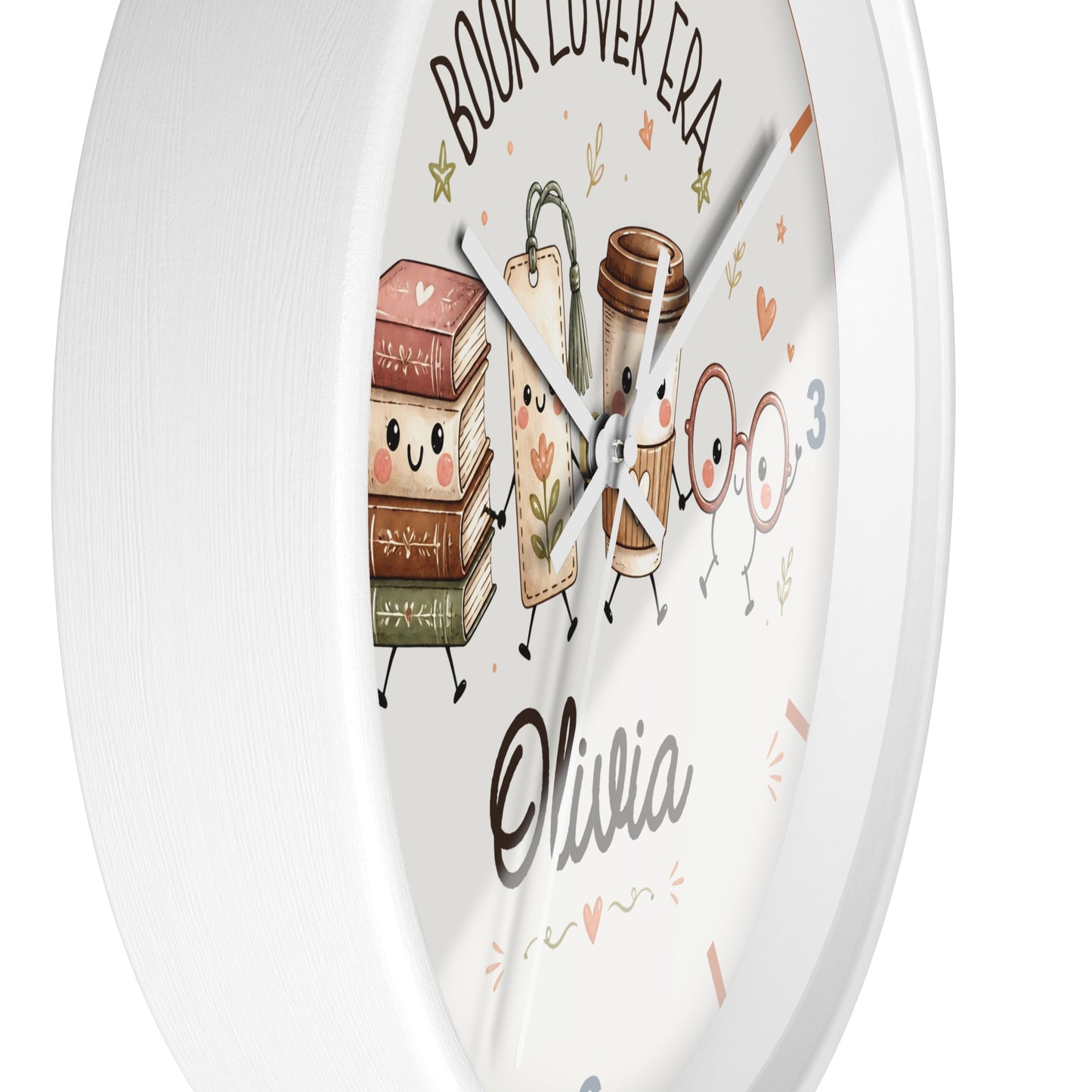 A round white wall clock with a cute cartoon book-themed design. The clock face features an illustration of smiling books, a coffee cup, and glasses, with the text 'BOOK LOVER ERA' at the top and the name 'Olivia' written in a cursive font near the bottom.