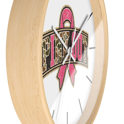 Round wall clock with a light natural wood frame and a white face featuring a pink ribbon and the word 'PINK OUT' in a camouflage pattern.