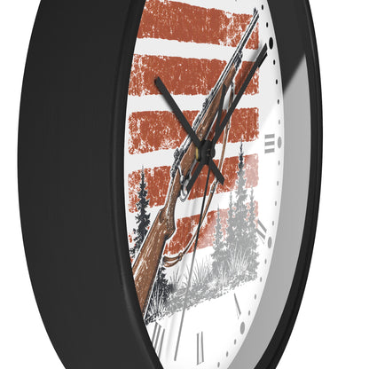 A close-up of a round wall clock with a black frame and a white face featuring a rustic orange and white striped design, a rifle illustration, and black hands.