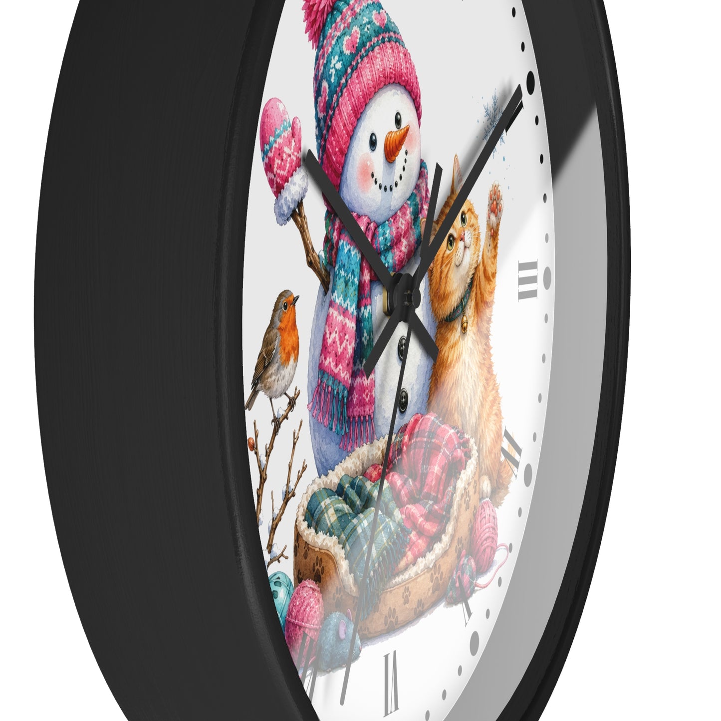 A round wall clock with a black frame and a white face featuring a winter illustration of a snowman, a cat in a sleigh, a small bird, and colorful knit hats and scarves.