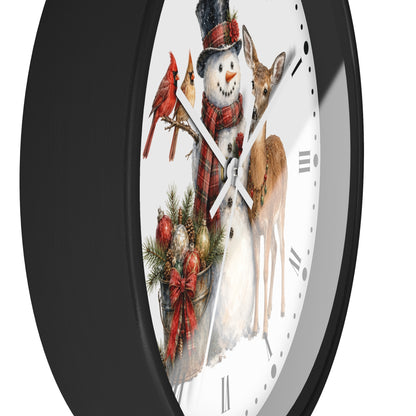 A round wall clock with a black frame and a white face featuring a winter holiday illustration of a snowman, a deer, two red cardinals, pine branches, ornaments, and a red plaid scarf.