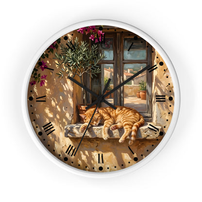 A round wall clock with a white frame and a printed illustration of an orange tabby cat sleeping on a stone windowsill in front of a sunlit Mediterranean-style window. The clock face includes black Roman numerals and hands, shown against a plain white background.