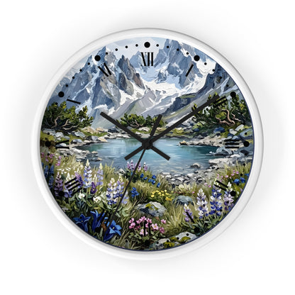 A round wall clock with a white frame and a scenic landscape print featuring snow-capped mountains, a lake, and wildflowers. The clock has black Roman numerals and black hands.