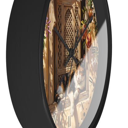 A round wall clock with a black frame and a printed illustration of a calico cat lounging by a wooden window, shown against a plain white background.