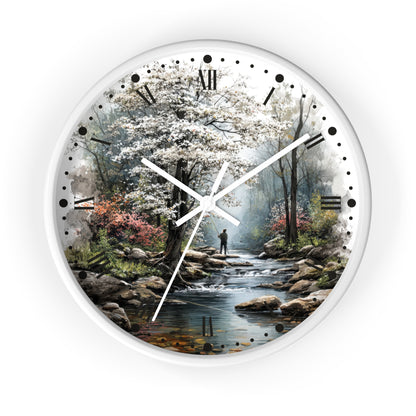Round wall clock with a white frame and a scenic print of a forest stream, cherry blossoms, rocks, and a small figure standing by the water. The clock has black Roman numerals and black dot hour markers with white hands.