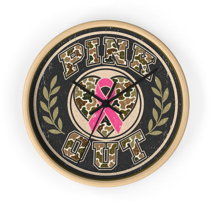 A round wall clock with a distressed design featuring the words 'PINK OUT' in camouflage lettering, a pink awareness ribbon in the center, and olive green laurel branches on a black background, surrounded by a light wood-toned frame.