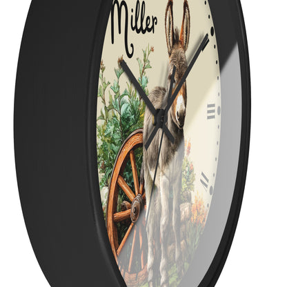 A round wall clock with a black frame and a printed front featuring a donkey, green plants, an orange wagon wheel, and the word 'Miller' at the top, shown against a plain white background.