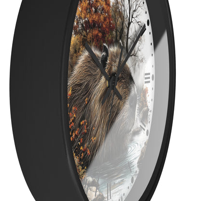 A round wall clock with a black frame and a printed nature scene featuring a capybara, autumn trees, and a snowy river on the face, shown against a white background.