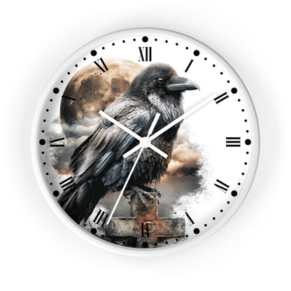 A round wall clock with a white outer frame and a printed design featuring a large black raven perched over a stone grave marker, with a cloudy sky and moon in the background. The clock face has black Roman numerals, black hour markers, and white hands.