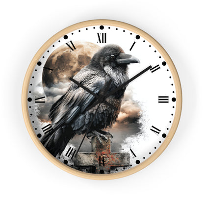 A round wall clock with a white frame and face, featuring a large black raven perched over a stone grave marker with a cloudy sky and moon background. The clock uses black Roman numerals and hour markers with black clock hands.