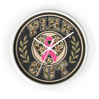 A round wall clock with a distressed design featuring the words 'PINK OUT' in a camouflage pattern, a pink ribbon in the center, and olive branch motifs on either side, all set against a black background with a white clock frame.
