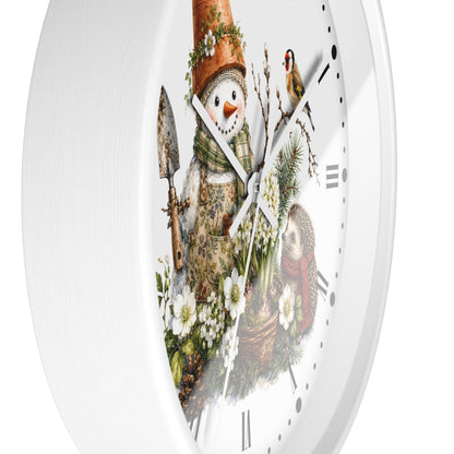 A white round wall clock with a whimsical winter garden illustration on the face, featuring a snowman in an apron with a gardening hat, flowers, a bird, and a basket, shown against a plain white background.