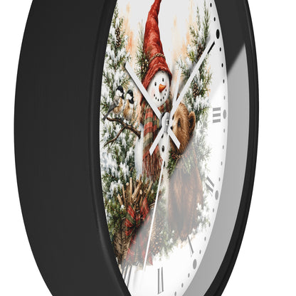 A round wall clock with a black frame and a white face featuring a winter illustration of a snowman in a red hat, birds, pine branches, and a brown bear.