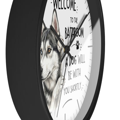 A round wall clock with a black frame and a white face featuring a husky illustration and the text 'WELCOME TO THE BATROOM A DOG WILL BE WITH YOU SHORTLY'.