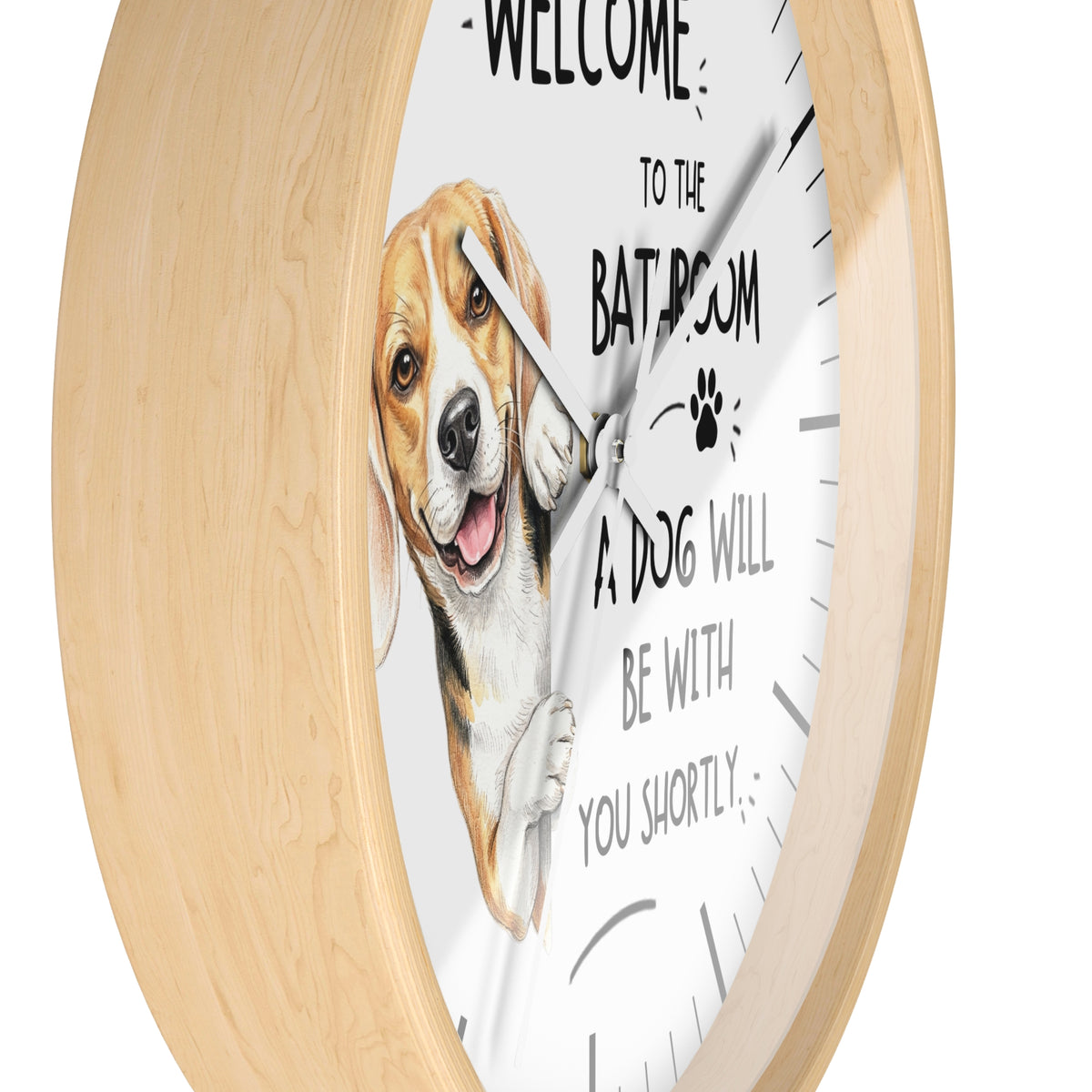 A round wall clock with a light natural wood frame and a white face. The clock face features a painted beagle dog illustration and the humorous text 'WELCOME TO THE BATHROOM A DOG WILL BE WITH YOU SHORTLY'.
