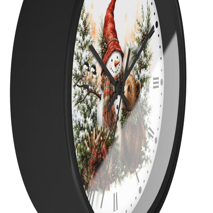 A round wall clock with a black frame and a white face featuring a winter illustration of a snowman in a red hat, evergreen branches, and a brown bear.