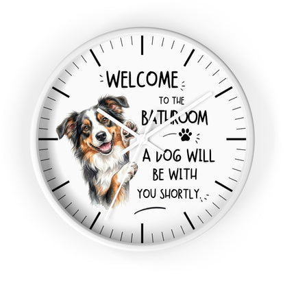 A round white wall clock with black hands and hour markers, featuring a watercolor illustration of a brown, white, and black dog next to the text 'WELCOME TO THE BATHROOM A DOG WILL BE WITH YOU SHORTLY.' on a white background.