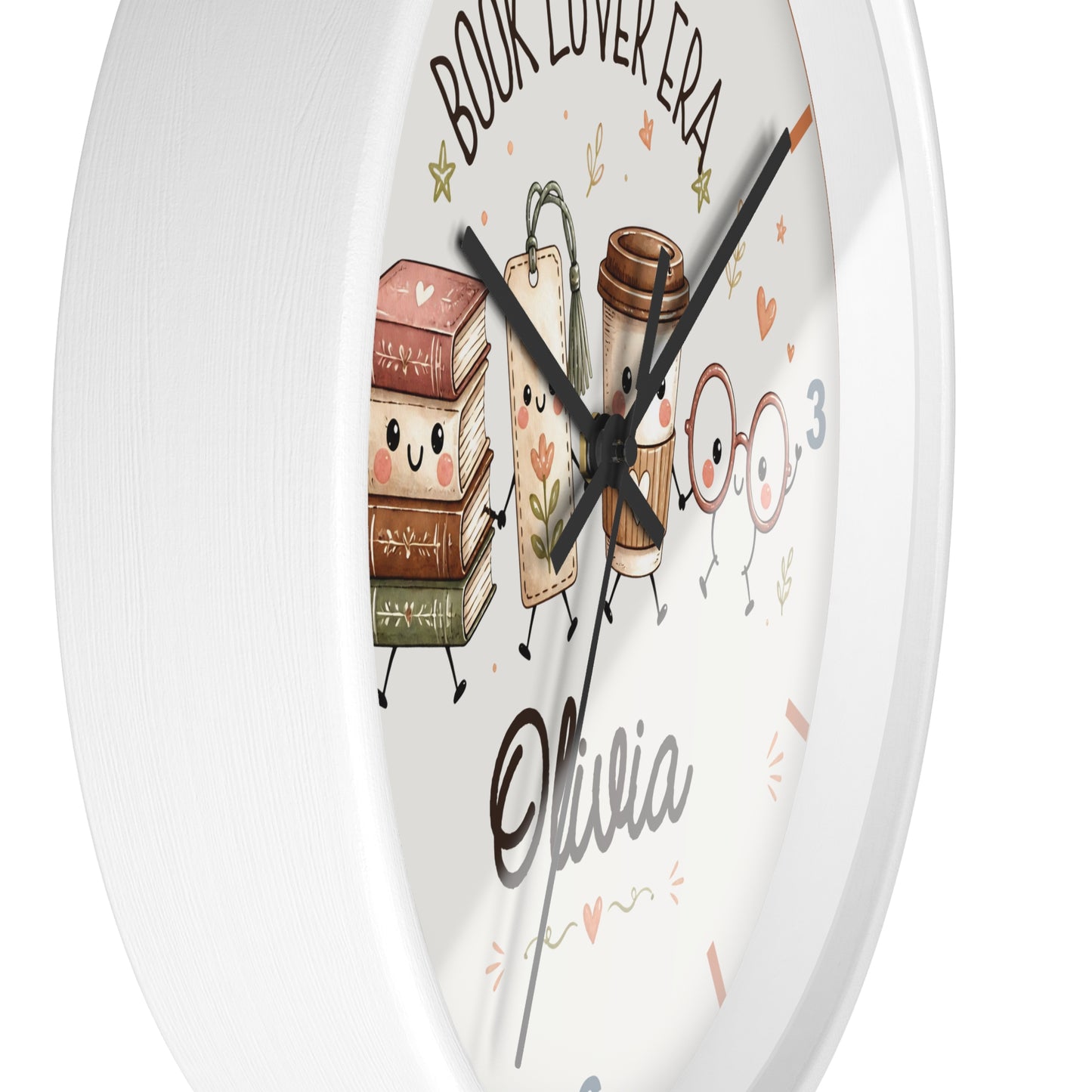A round white wall clock with a cute book-themed illustration. The clock face features cartoon books, a coffee cup, and two glasses of juice with faces, along with the text 'BOOK LOVER ERA', the name 'Olivia', and decorative doodles in pink and gold.