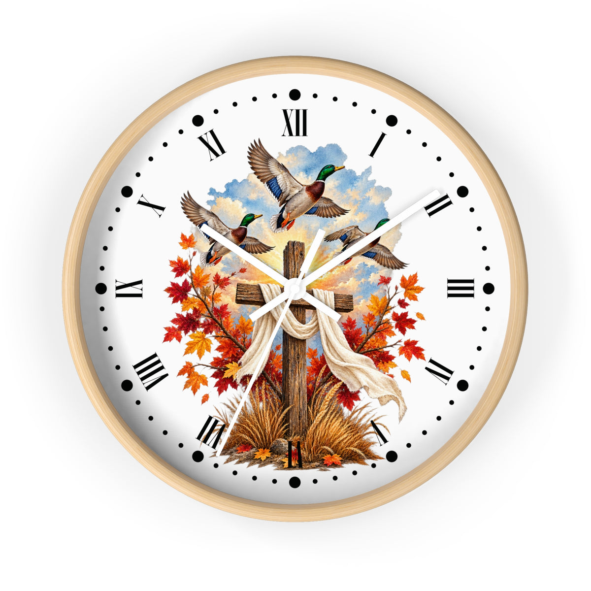 A round wall clock with a light wood frame and a white face, featuring a printed design of three mallards flying above a wooden cross draped with a white cloth, surrounded by red and orange autumn leaves and grass. The clock has black Roman numerals and white hands, shown against a plain white background.