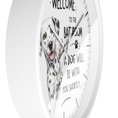 A white round wall clock with a printed illustration of a Dalmatian dog and the humorous text 'WELCOME TO THE BATROOM A DOG WILL BE WITH YOU SHORTLY' on a clean white background.